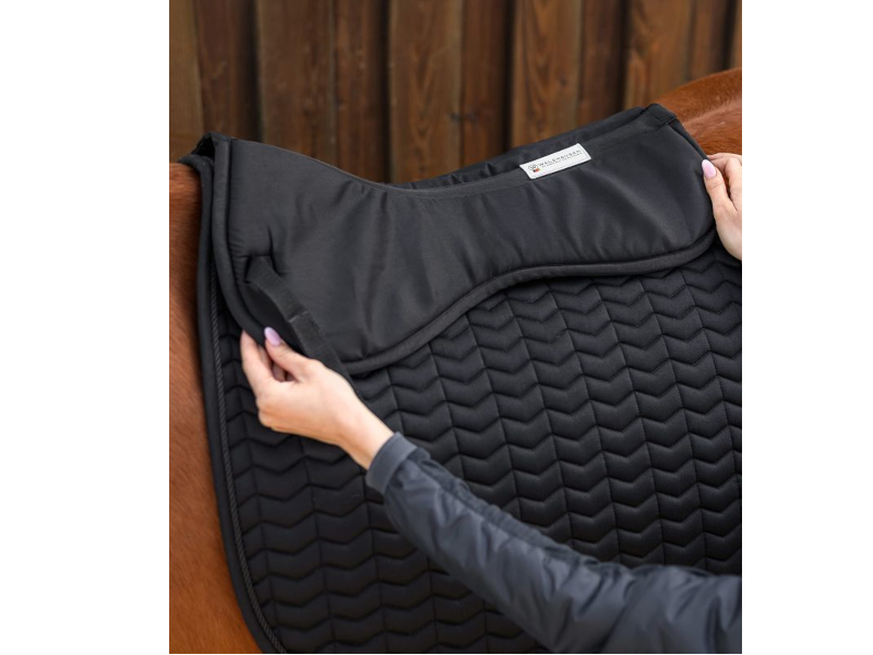 Hände legen schwarzes Sattelkissen auf einen Pferderücken mit schwarzer Satteldecke