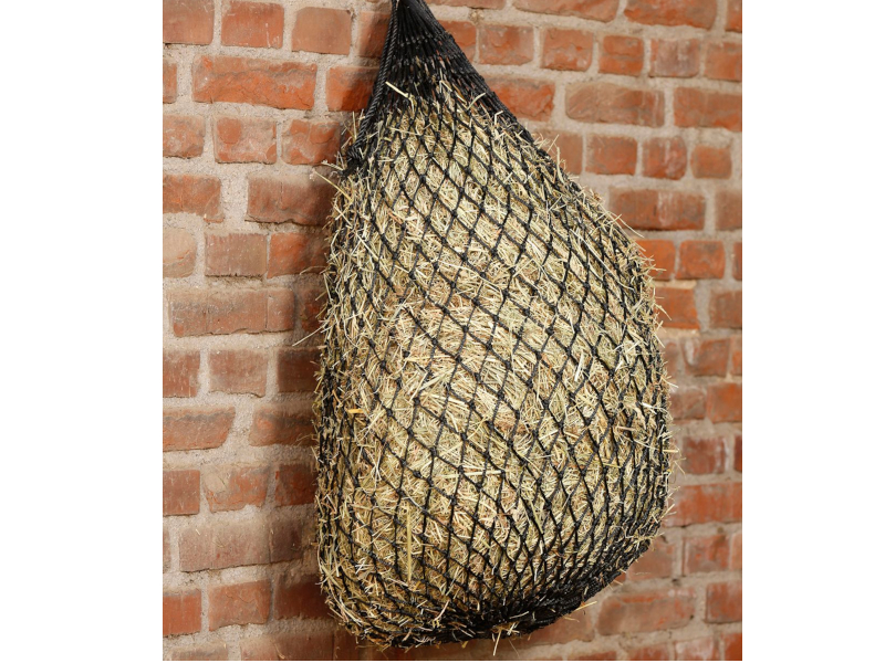 schwarzes Heunetz gefüllt mit Heu hängt an Ziegelwand